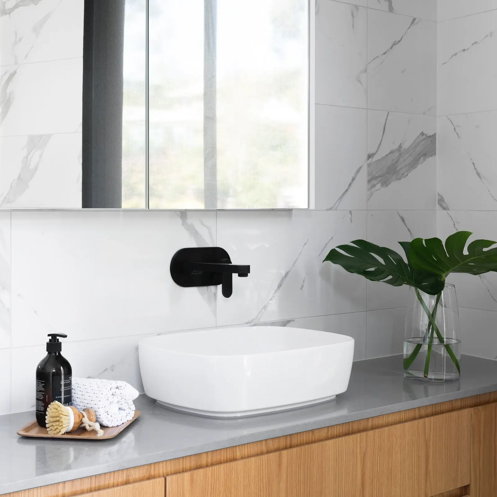 Modern bathroom with marble-look tiles, timber vanity, black tapware and above-counter basin