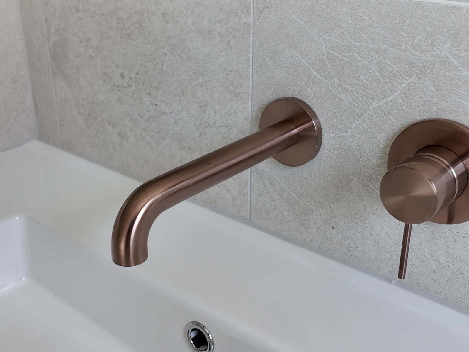 Close-up of the Nero Mecca wall basin mixer and spout in brushed bronze above the ceramic basin