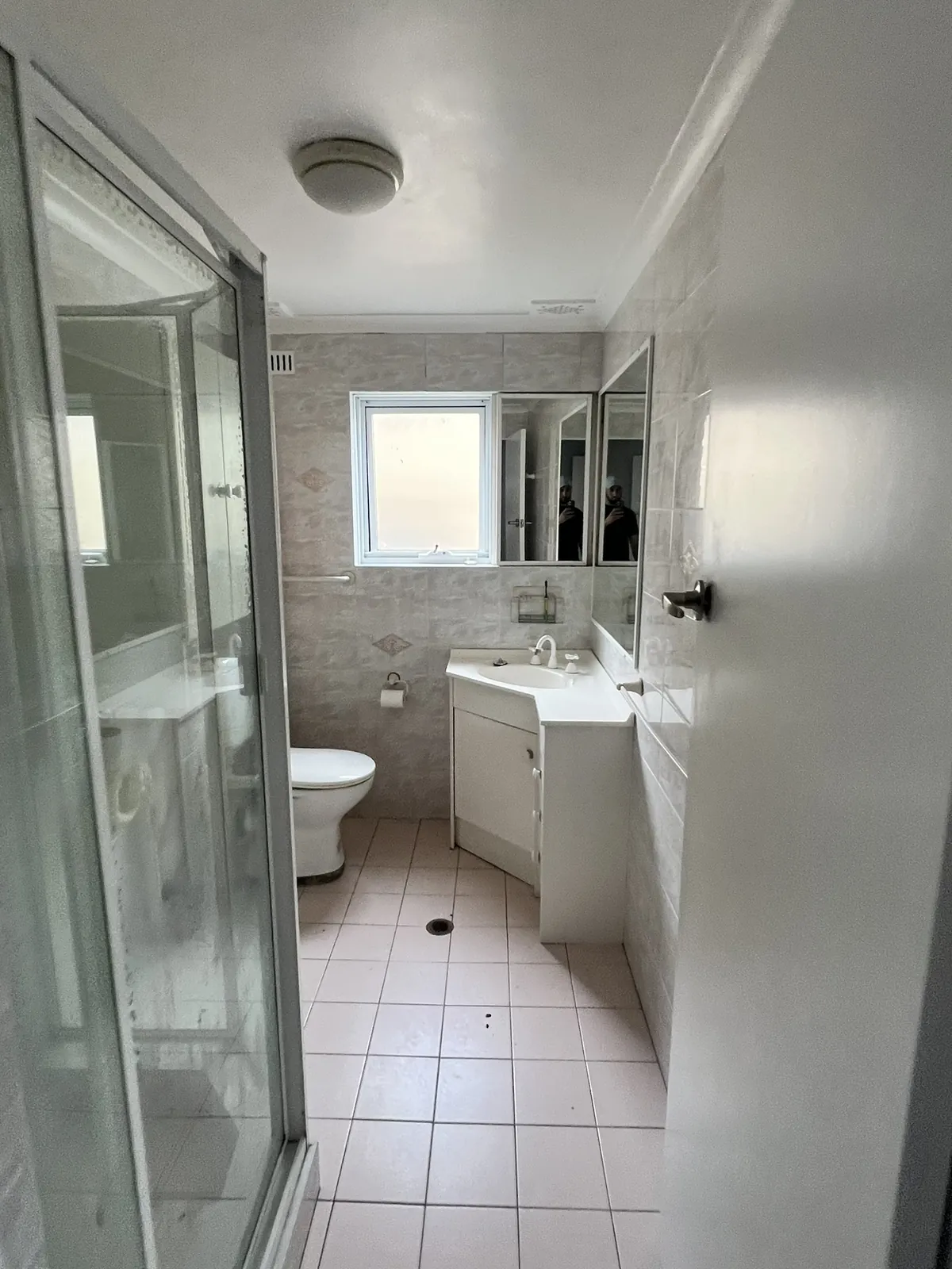 The original Coogee apartment bathroom before renovation, with a framed corner shower screen, pink floor tiles and a laminate vanity