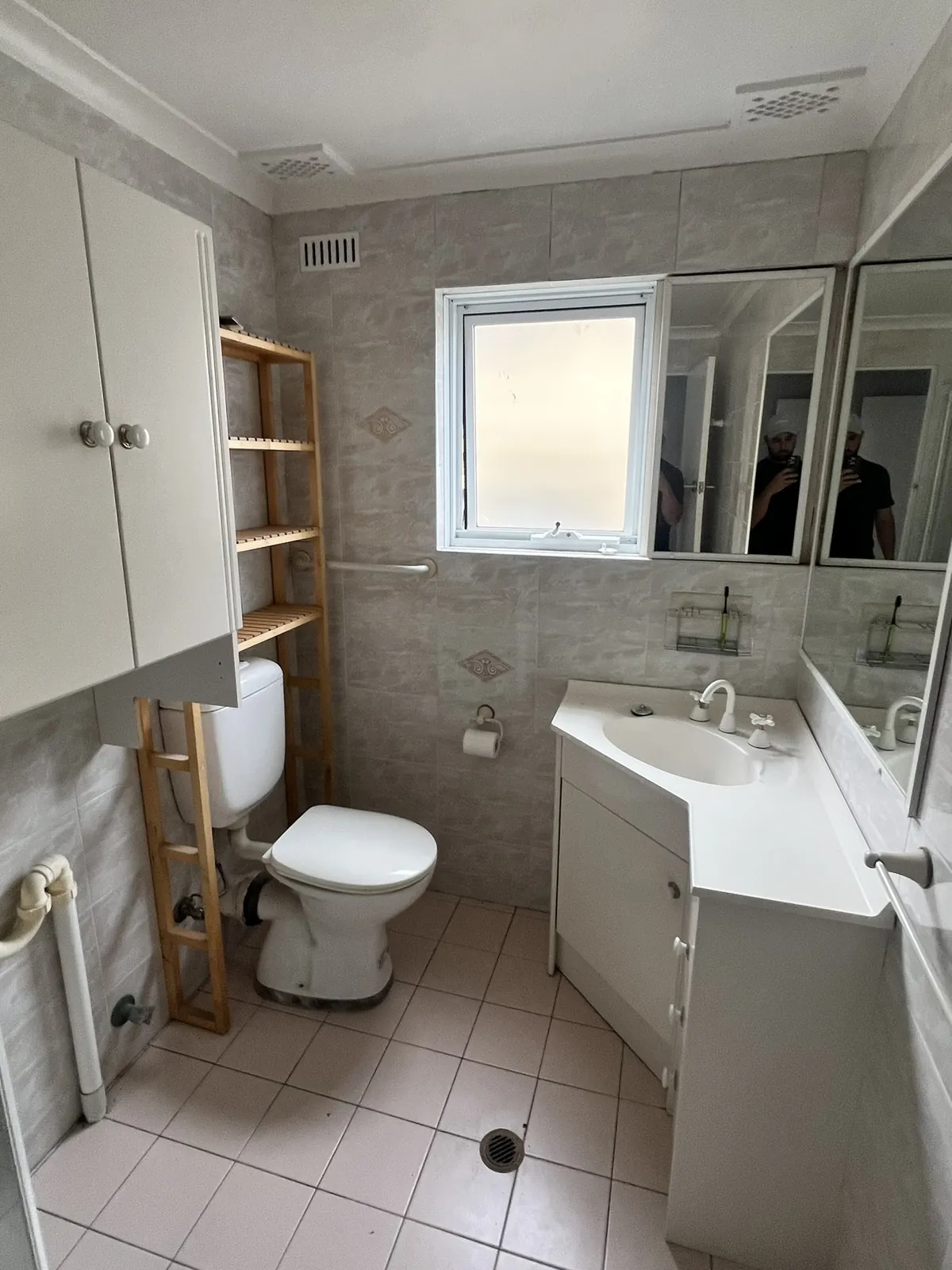The original bathroom before renovation, looking towards the vanity, with an over-toilet shelf unit and dated wall tiles
