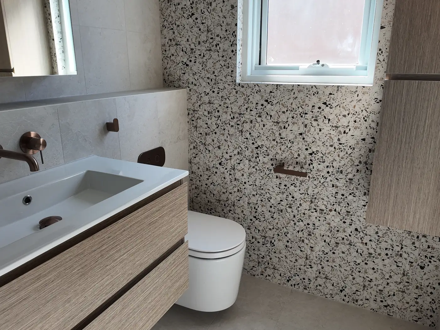 Terrazzo-look feature wall running behind the toilet and window in the renovated Coogee bathroom