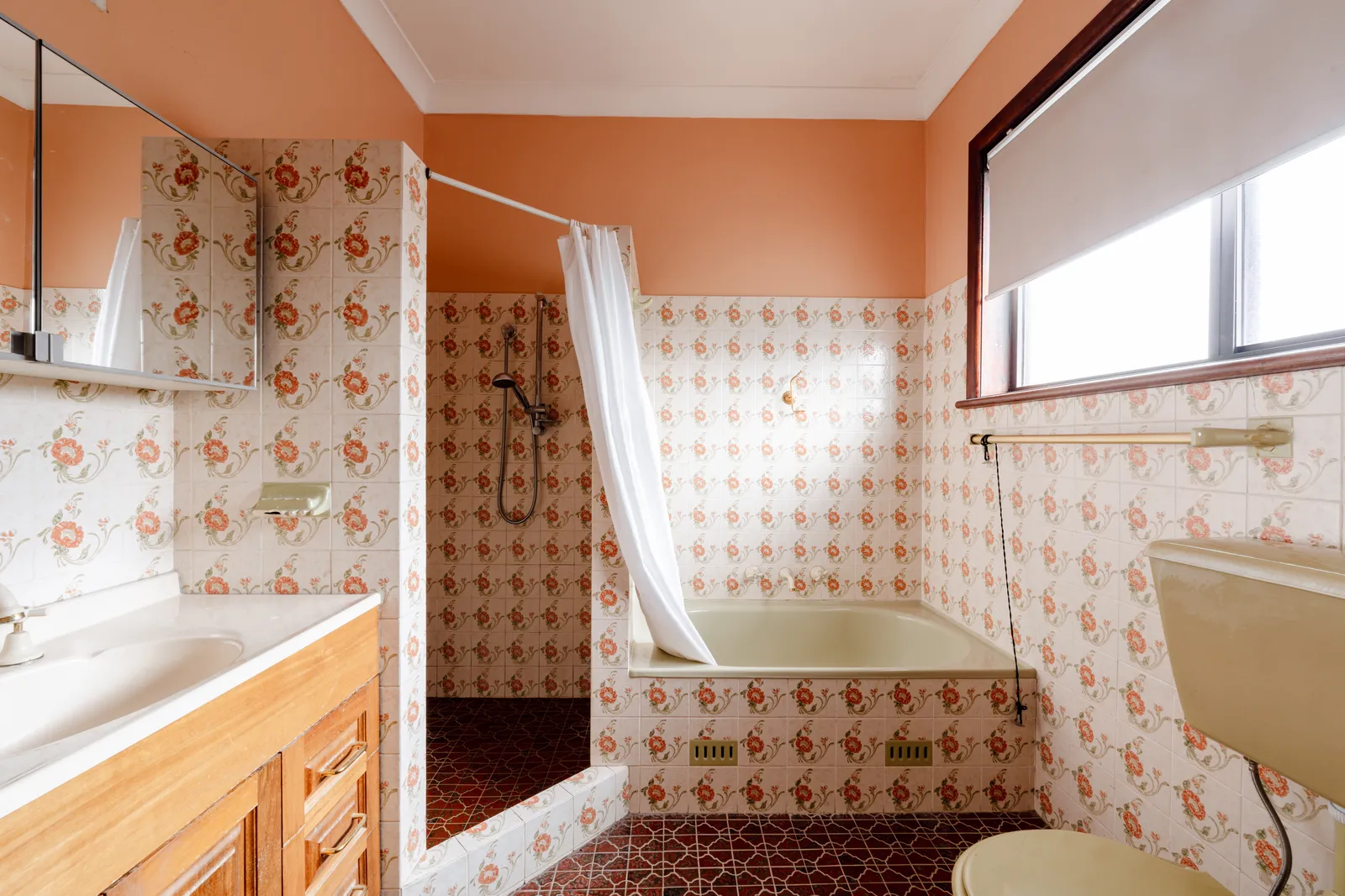 Original Mount Pritchard ensuite with orange walls, floral tiles, shower curtain, and built-in bathtub