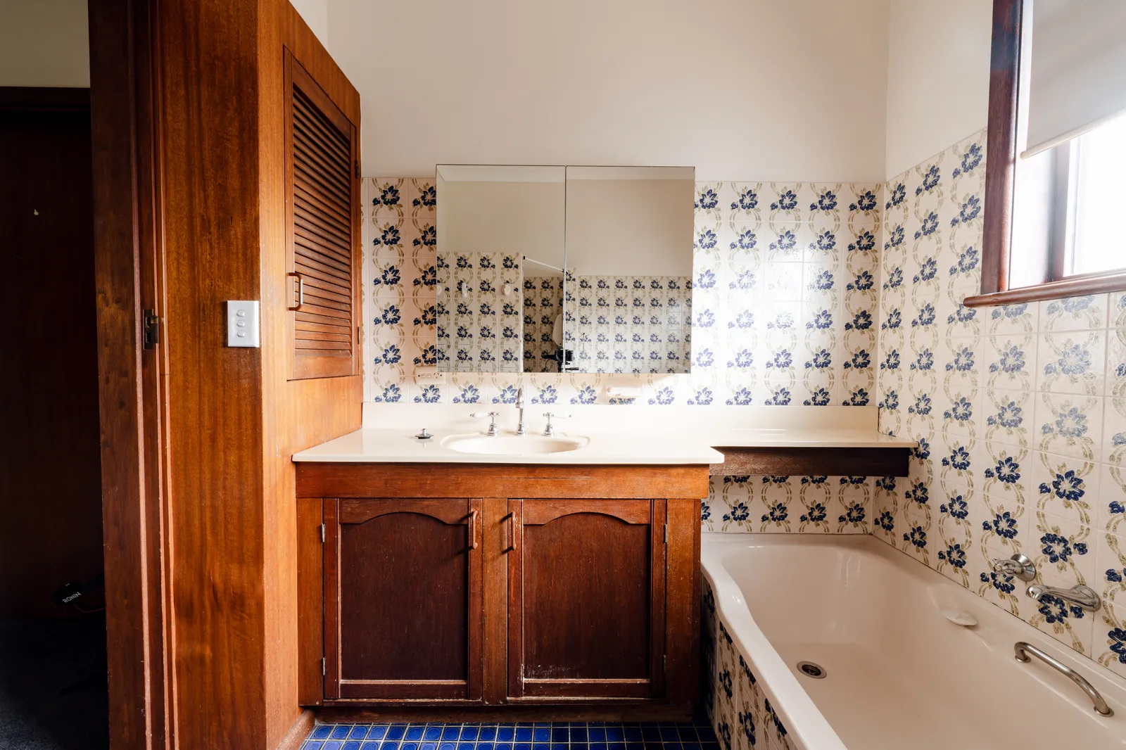 Original Mount Pritchard main bathroom with blue floral tiles, timber vanity, and built-in bathtub
