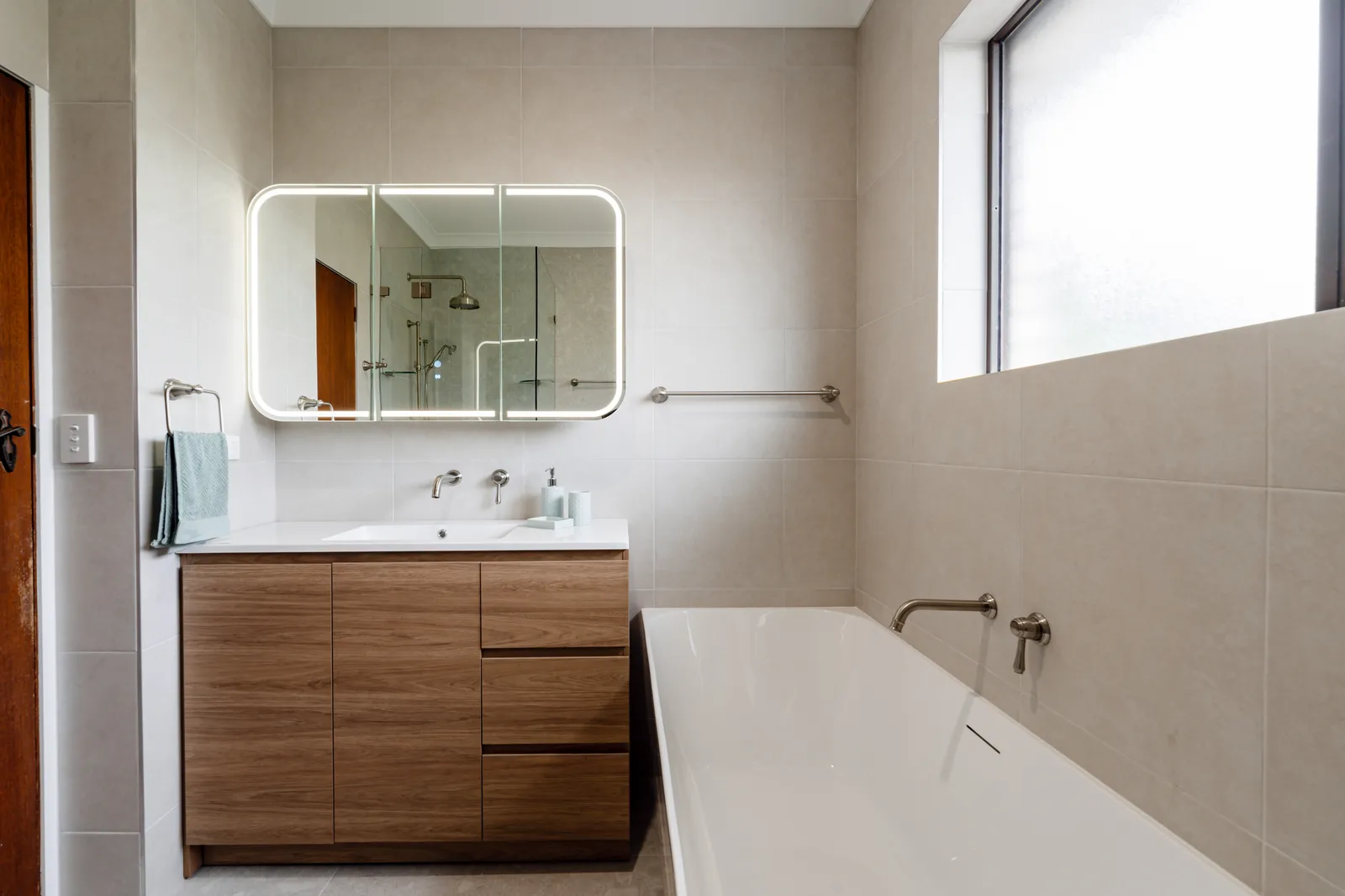 Main bathroom with timber vanity, LED backlit mirror cabinet, back-to-wall bathtub and brushed nickel tapware
