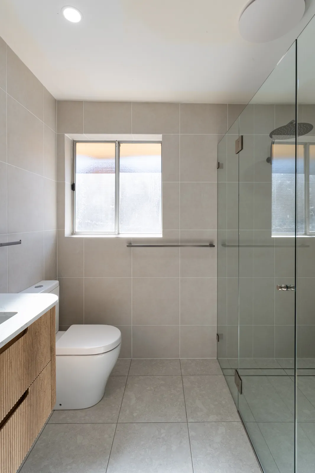 New bathroom with fluted vanity, walk-in shower and floor-to-ceiling tiling