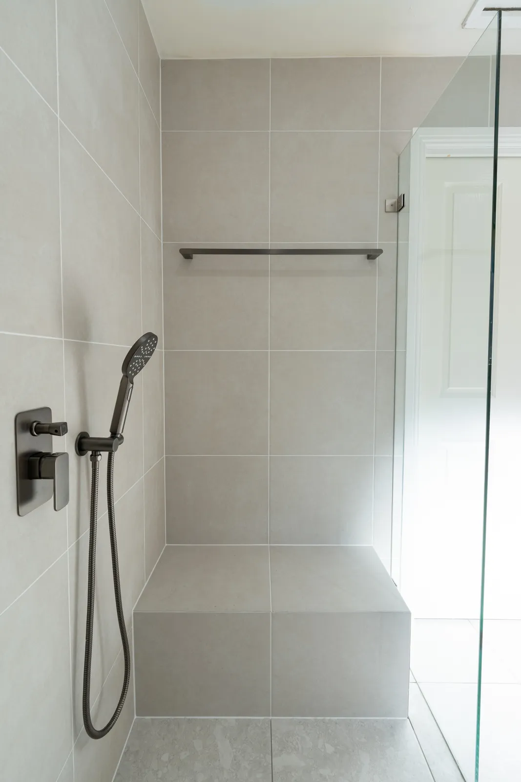 Walk-in shower with full-width tiled bench seat and gunmetal handheld shower