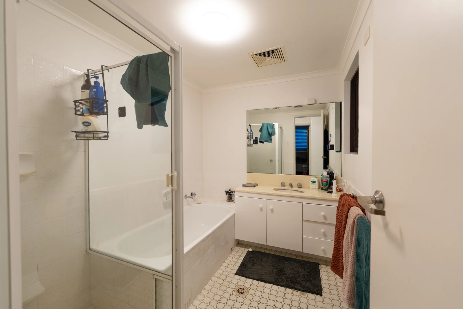The original Wollstonecraft bathroom before renovation, with a built-in bath, patterned floor tiles and a laminate vanity