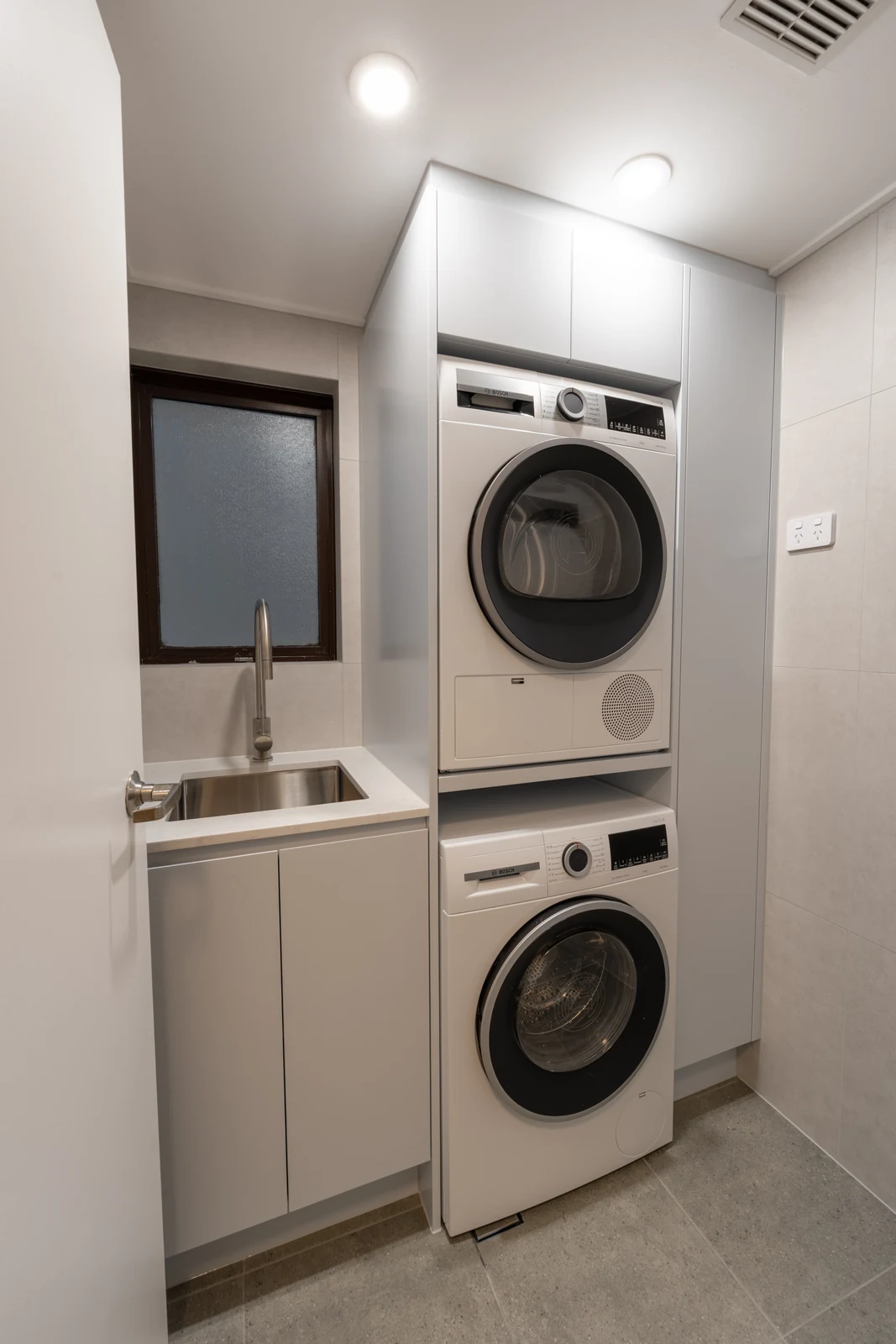 Renovated apartment laundry in Wollstonecraft with stacked Bosch appliances in a full-height cabinet and stone benchtop