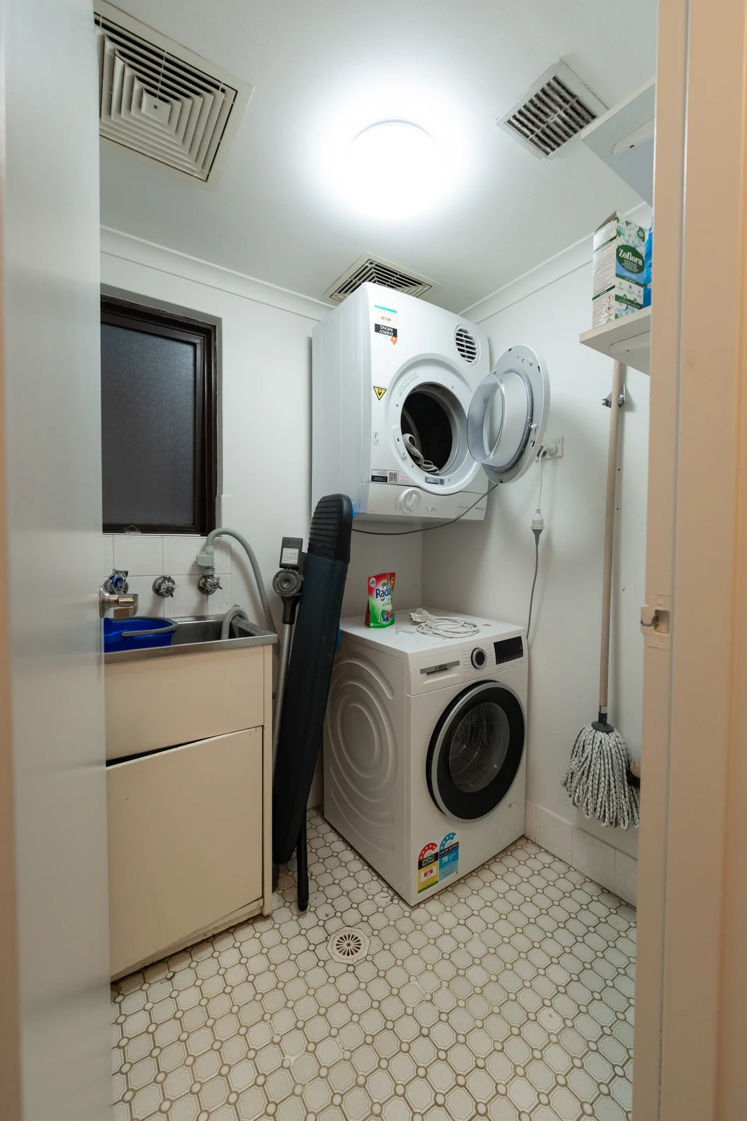 The original apartment laundry before renovation, with a freestanding washing machine, wall-mounted dryer and a laminate trough cabinet