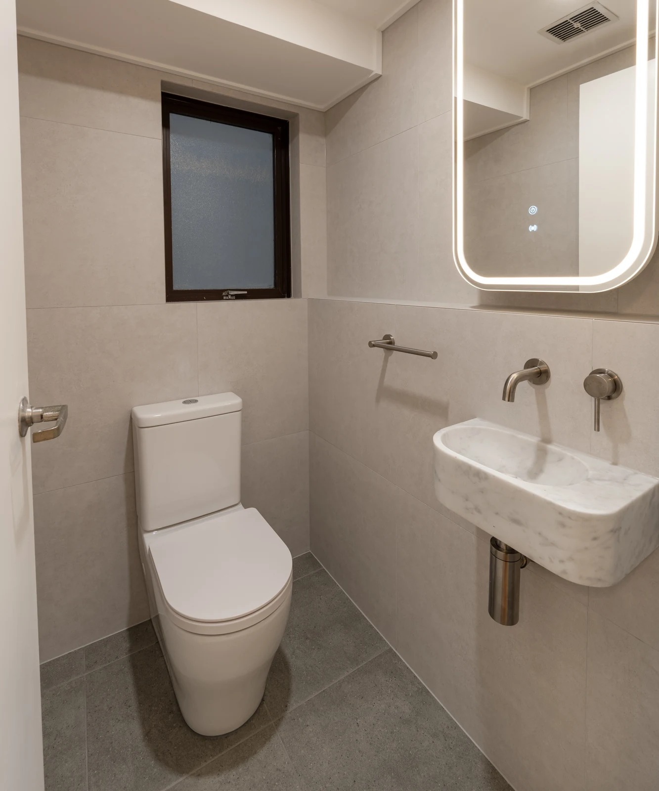 Renovated powder room in Wollstonecraft with wall-hung Carrara marble basin and backlit mirror