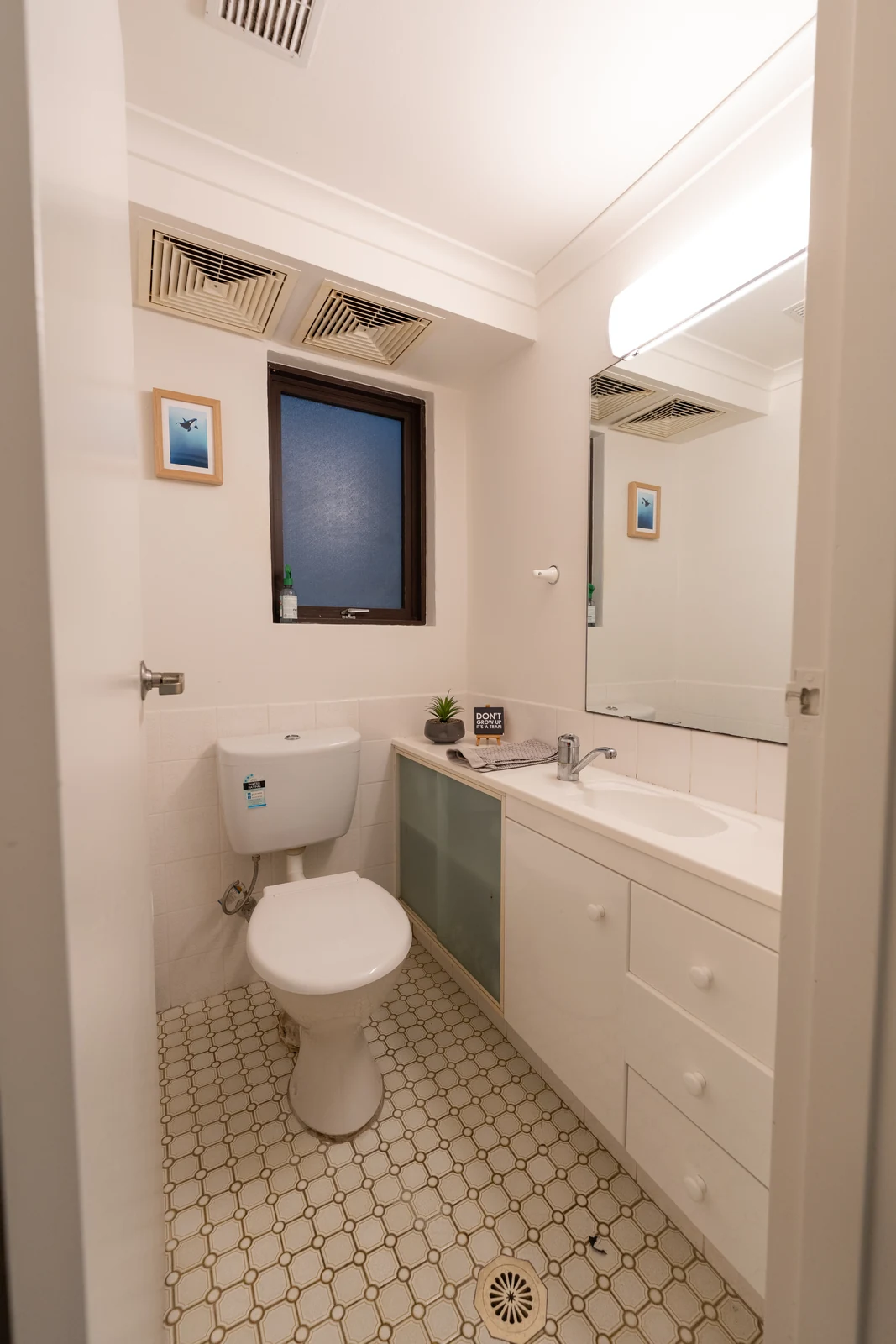 The original powder room before renovation, with a laminate vanity, patterned floor tiles and a fluorescent light