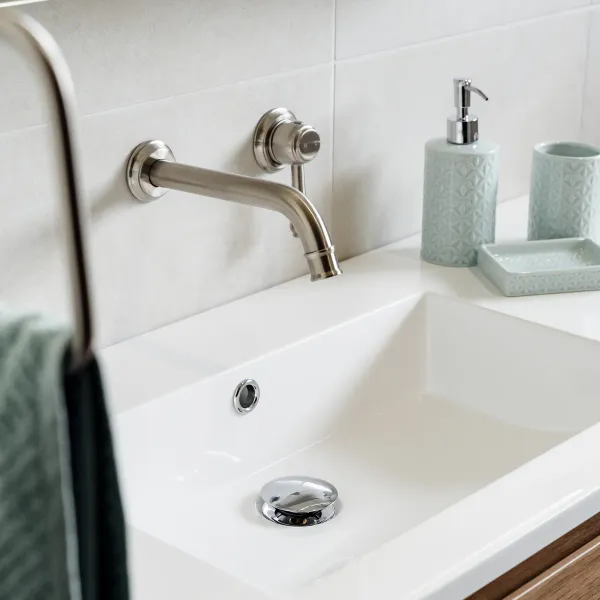 Wall-mounted brushed nickel basin tap with white countertop and timber vanity drawers